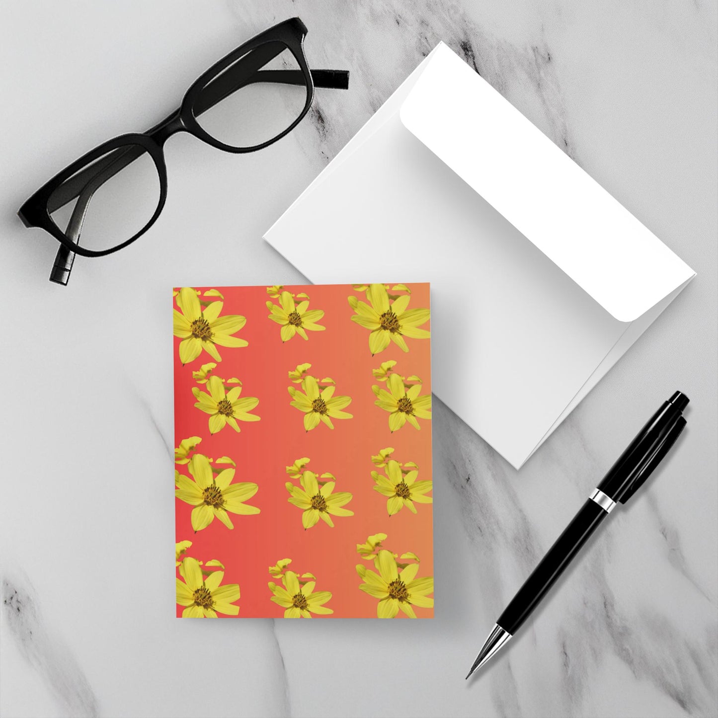 Greeting card with yellow floral pattern on red background with a white envelope, glasses, and pen on marble surface