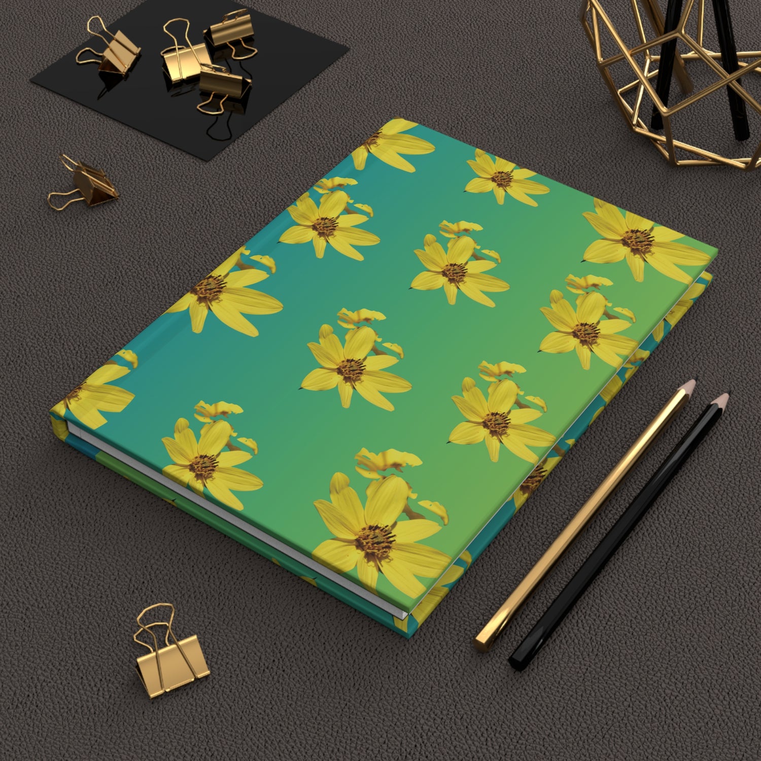 Notebook with yellow flower pattern on a green background on a dark surface with office supplies.