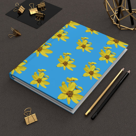 Notebook with yellow flower pattern on a blue background, surrounded by office supplies on a dark surface.