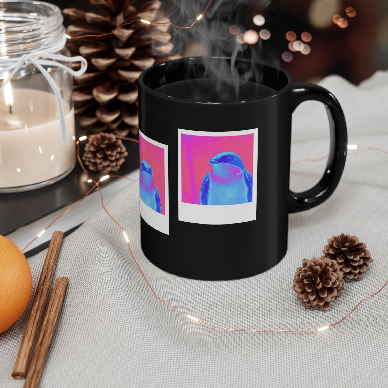 Black mug with colorful design featuring 3 polaroids of a  blue bird with a pink background surrounded by decorative items on a table.