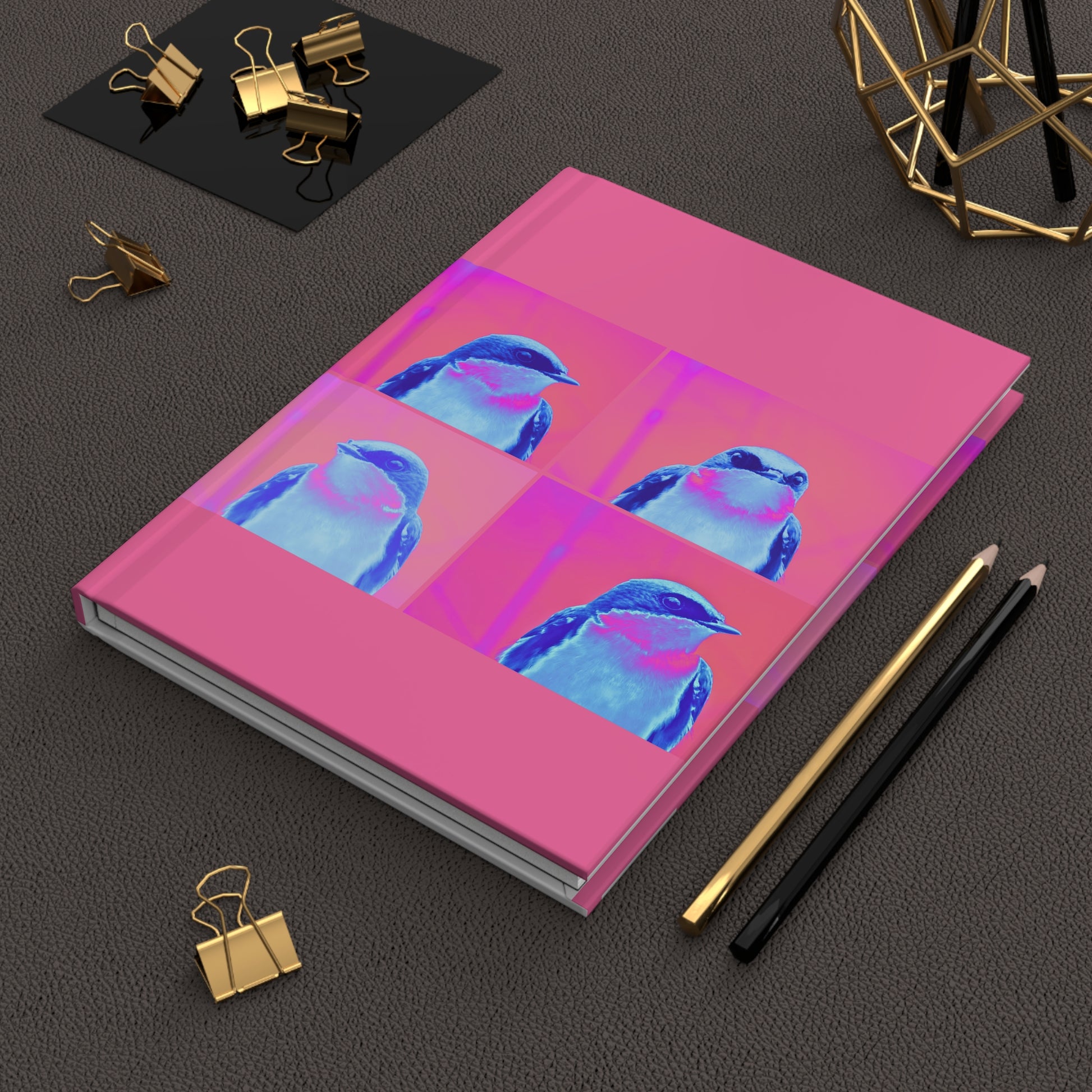 Pink notebook with blue bird design on a dark surface with office supplies.