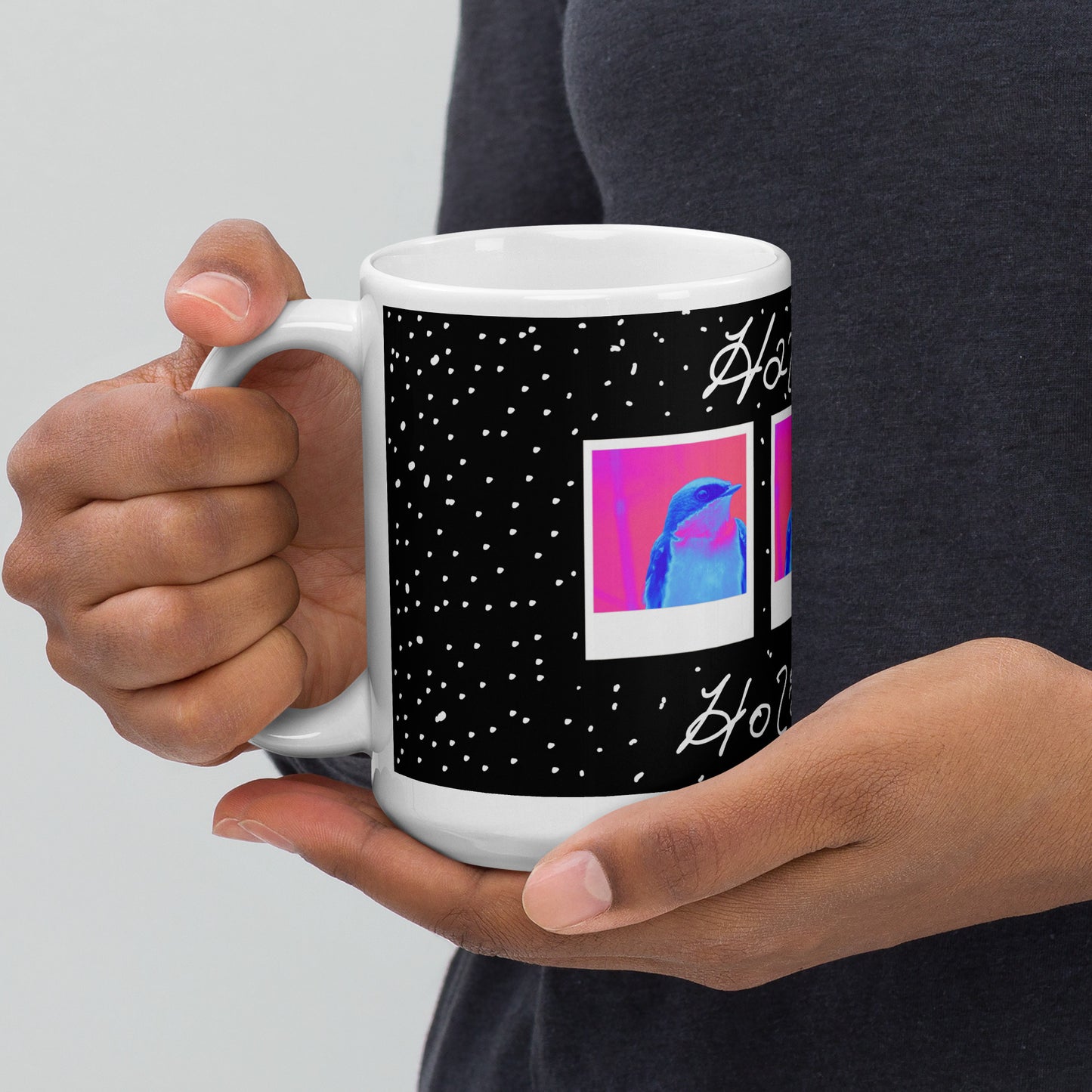 Person holding a mug with a black design featuring a colorful bird illustration and "Happy Holidays" text. 